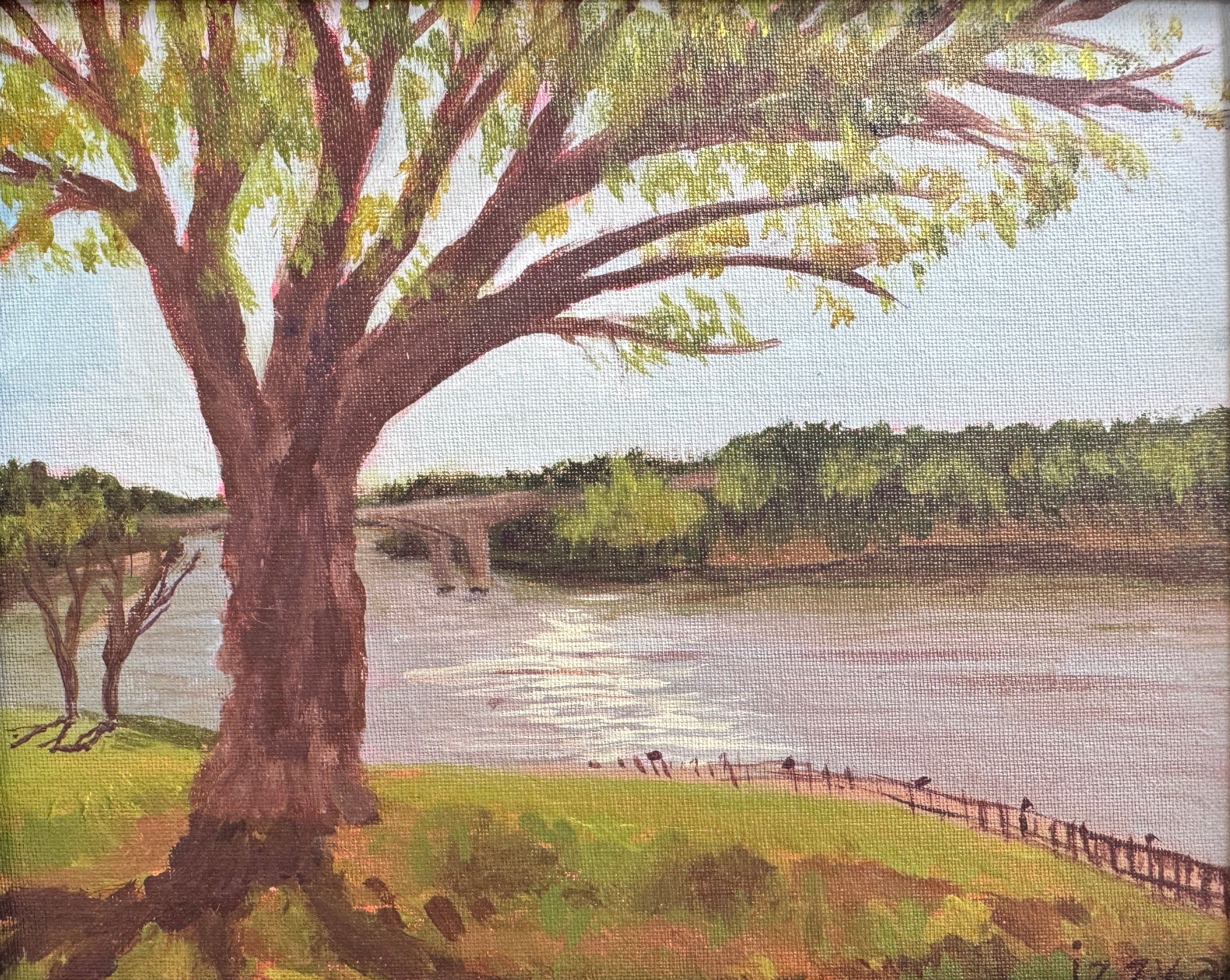 Framed painting of a tree by a lake with a bridge in the background.